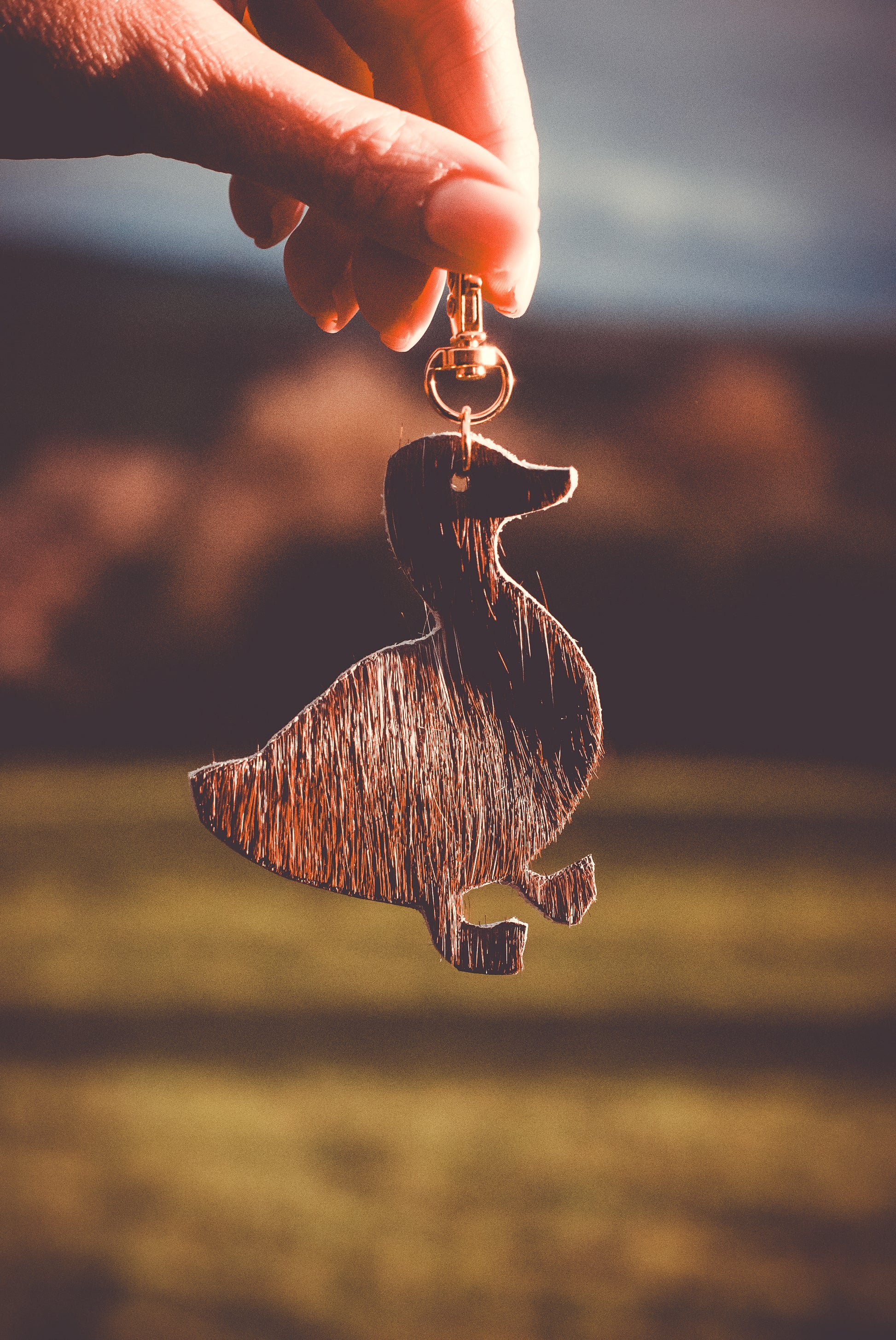 Speckled fabric farmyard animal keyring with gold ring held up in sunlight