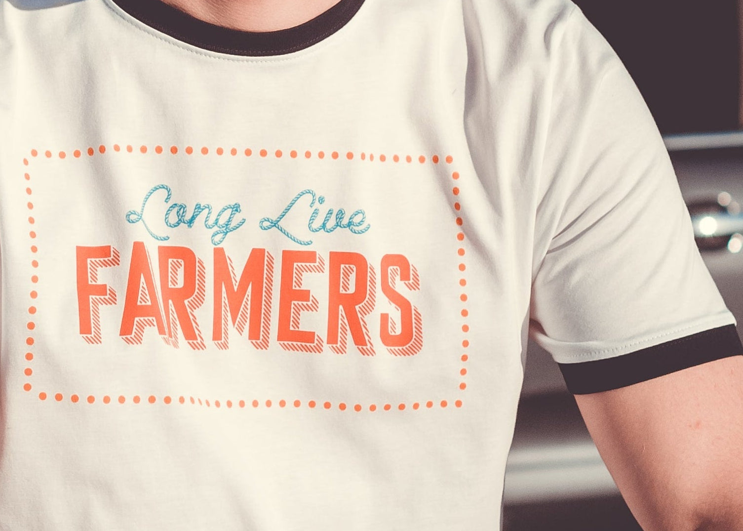 Man wearing a t-shirt with 'Long Live Farmers' text, sitting by a car in a scenic outdoor setting.