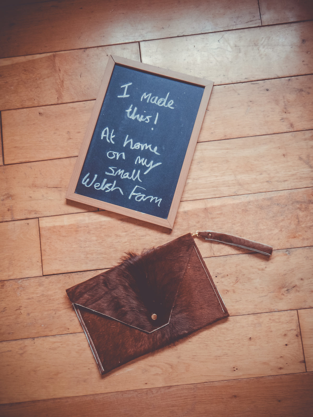 Brown cowhide envelope clutch with front flap and snap button, long wrist strap