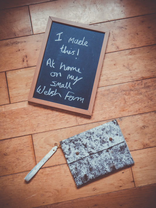 Cowhide clutch bag with wrist strap on wooden floor, mottled gray speckled pattern.