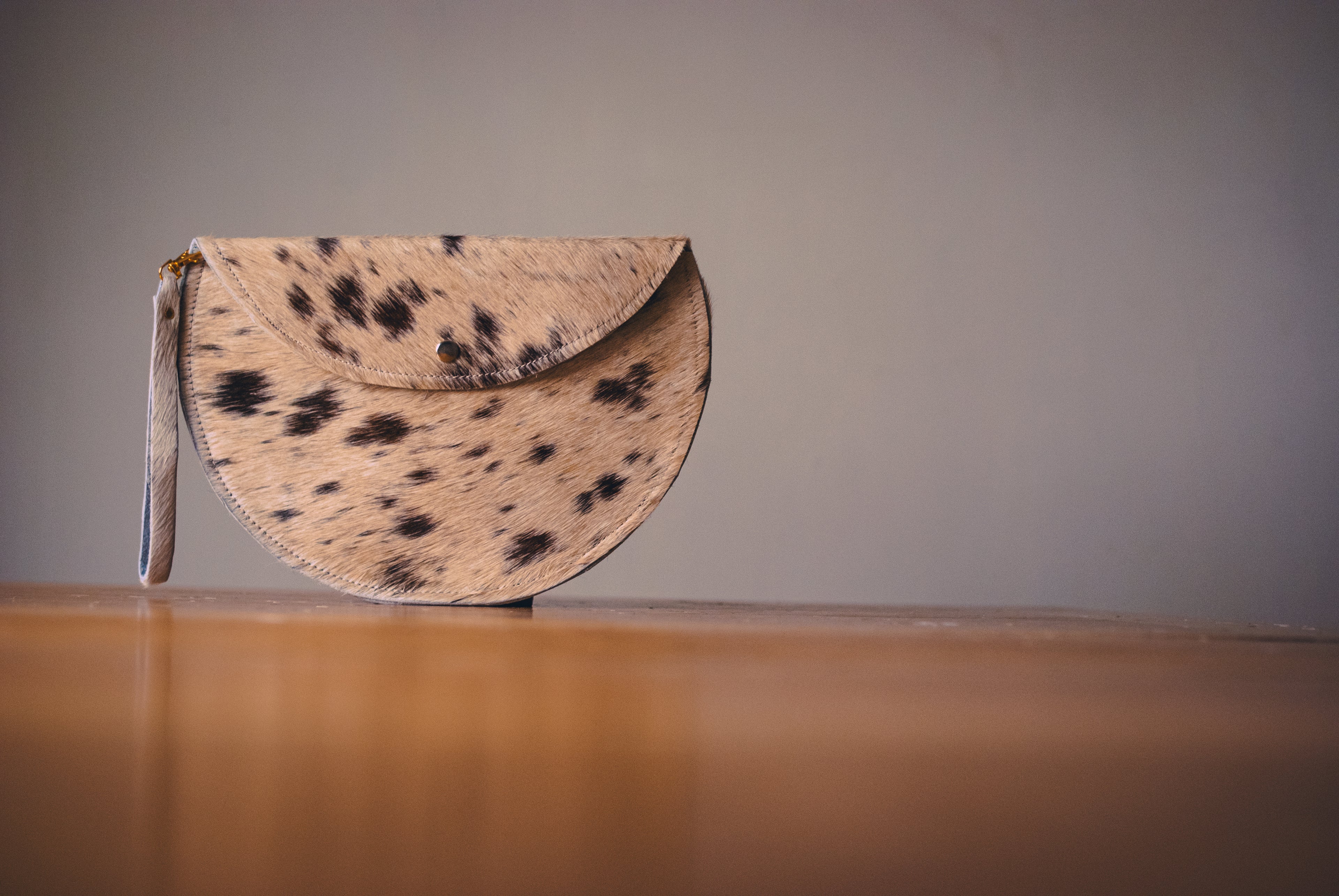 Calf hair clutch bag with black spots on a wooden surface and gray background