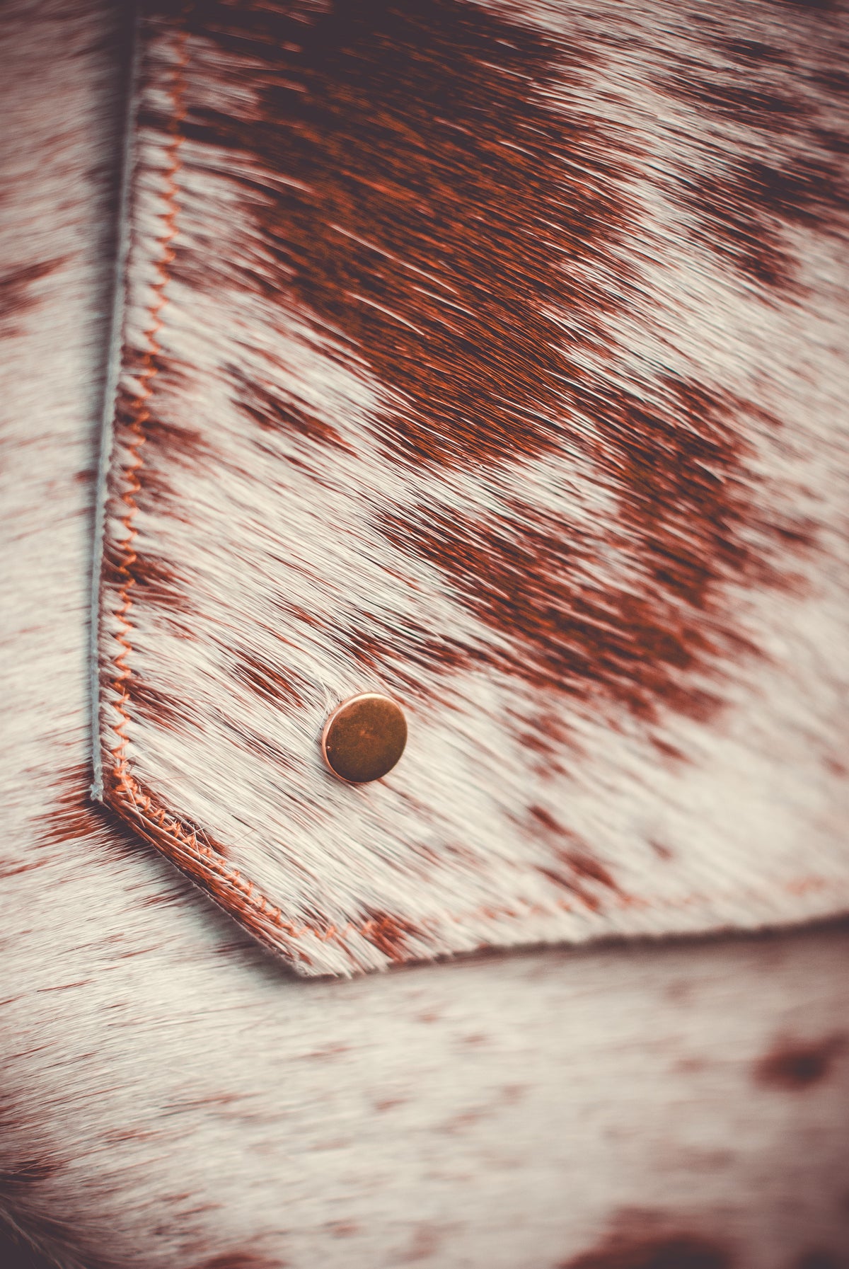 Cowhide clutch detail with brown-and-white spots and round snap button