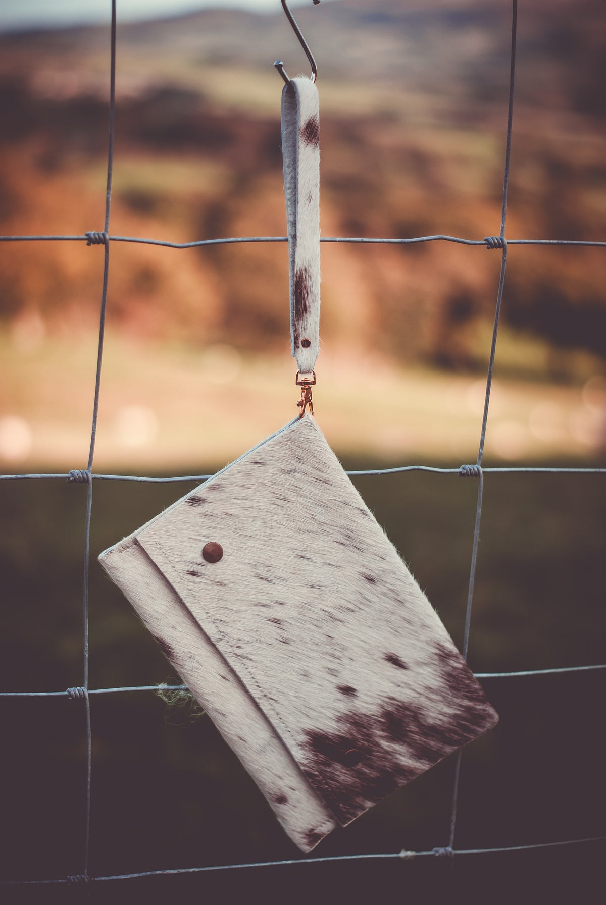 White and brown cowhide clutch bag with snap button and hanging wrist strap