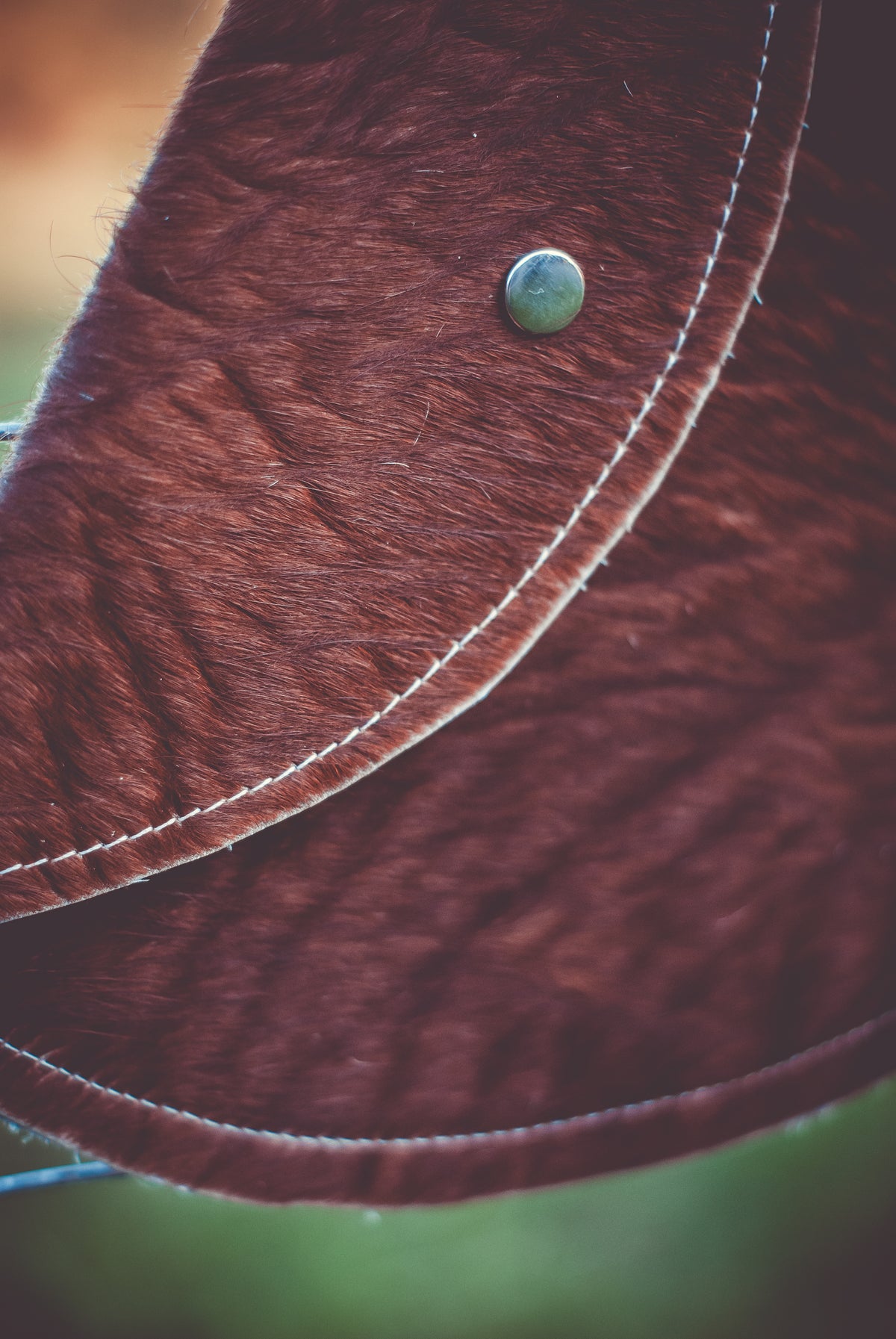 Close-up of brown cowhide moon clutch with curved stitched trim and round snap