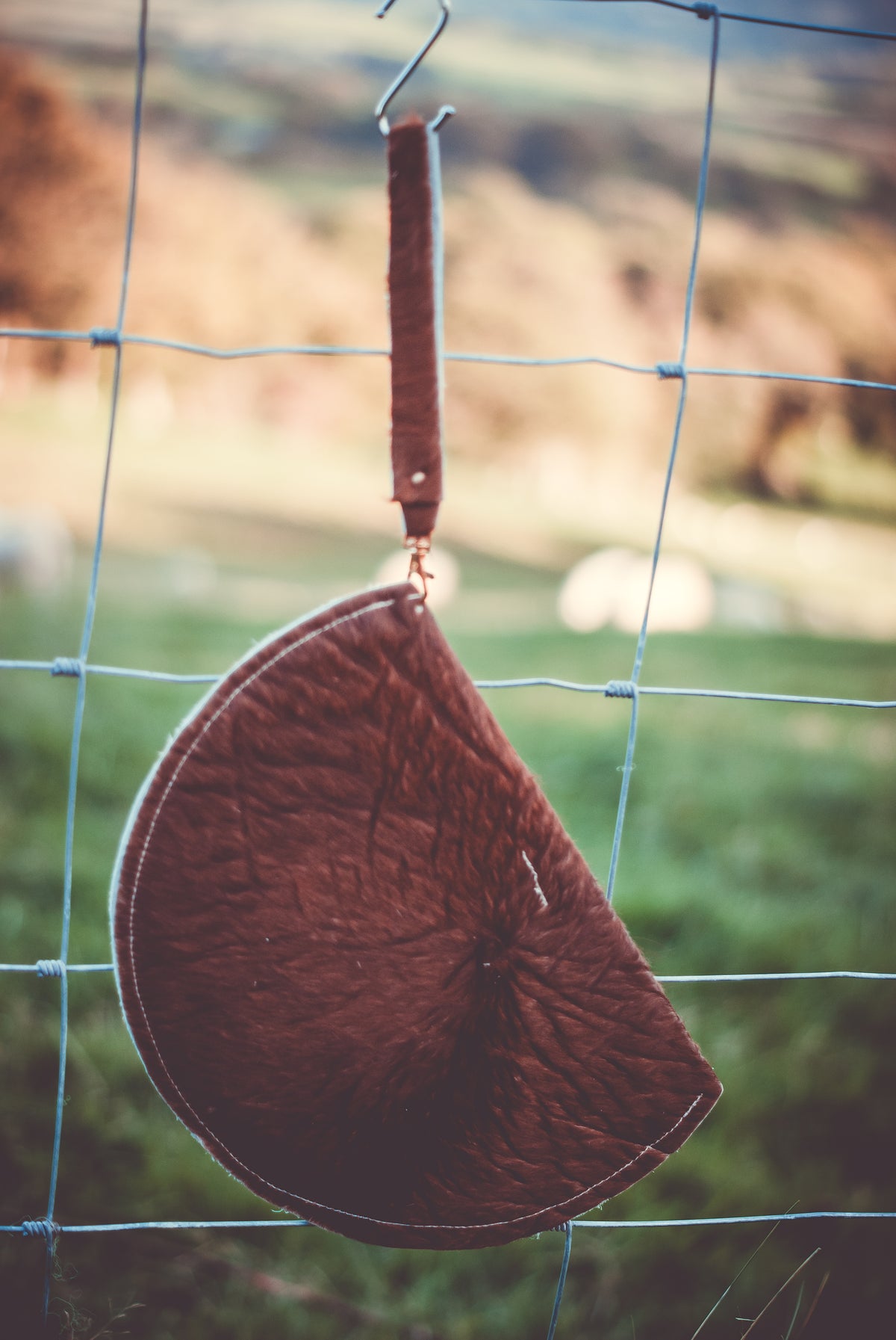 Brown cowhide moon clutch bag hanging with contrast piping and snap button