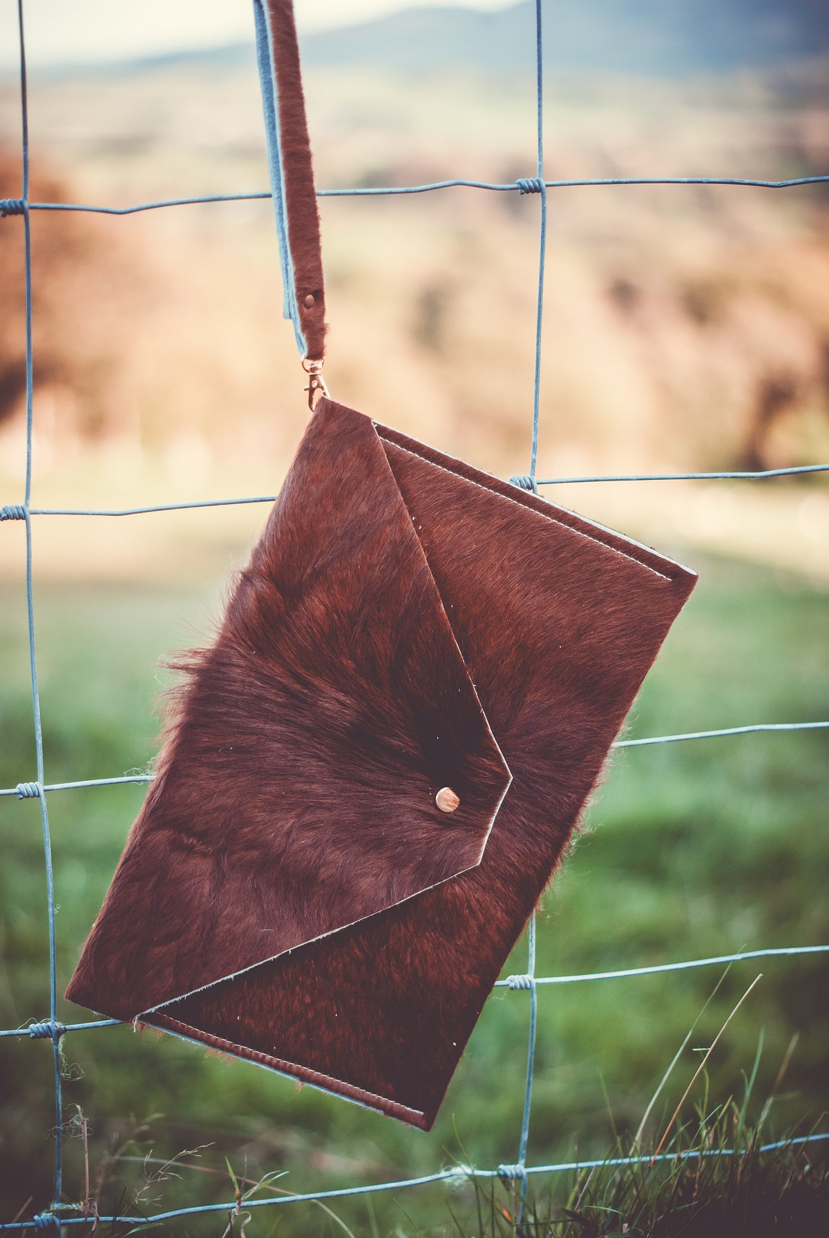 Brown cowhide envelope clutch bag with top flap and snap closure, blue wrist strap