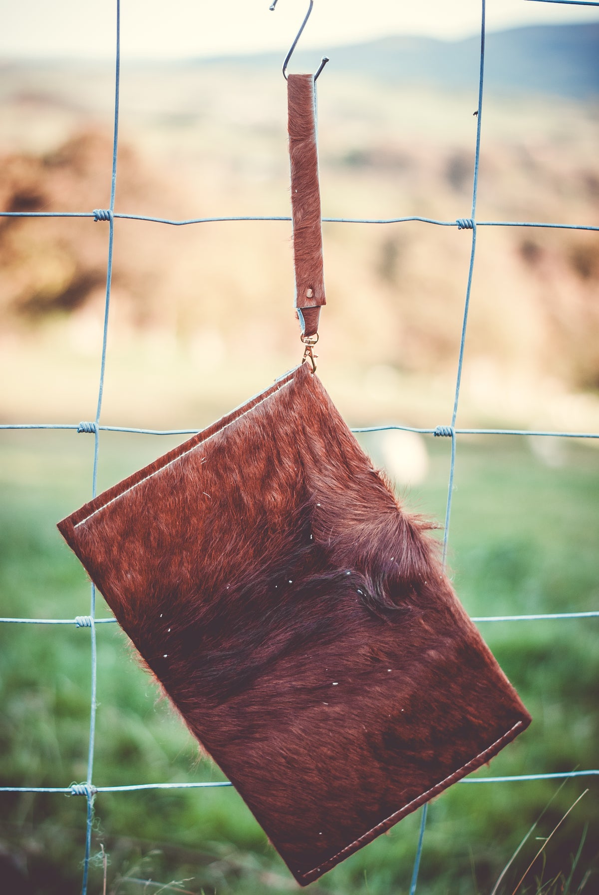Brown cowhide envelope clutch with front flap and blue strap, one-button closure
