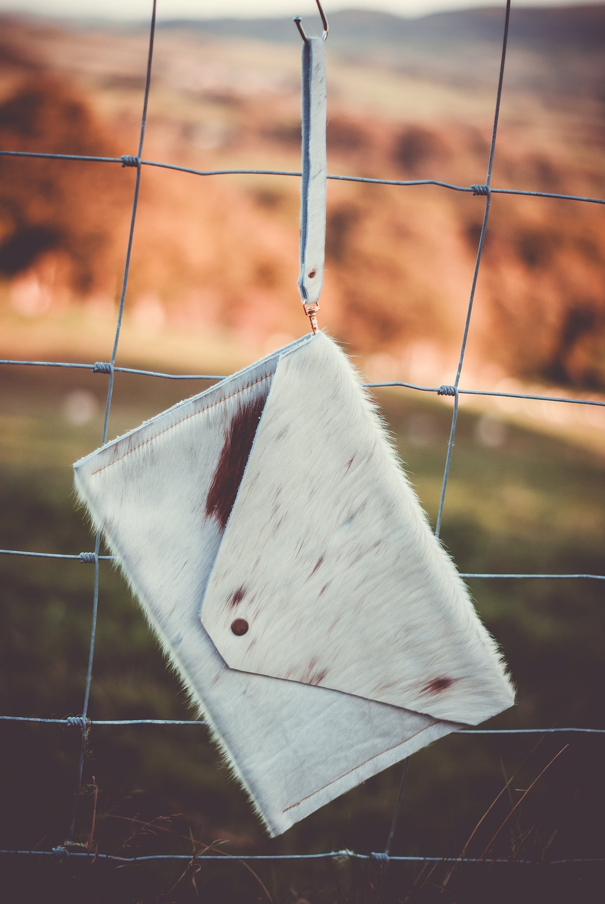 Cowhide envelope clutch bag with light fur and dark spots, wrist strap