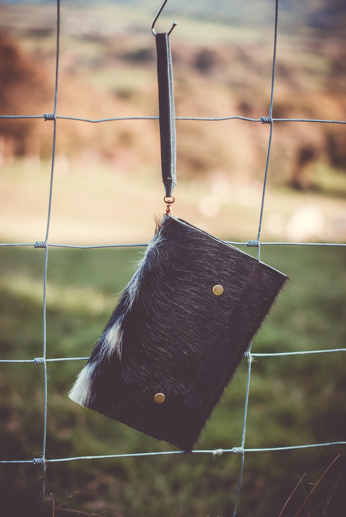 Cowhide clutch bag with fur-trim flap, brass snap buttons, hanging loop strap.