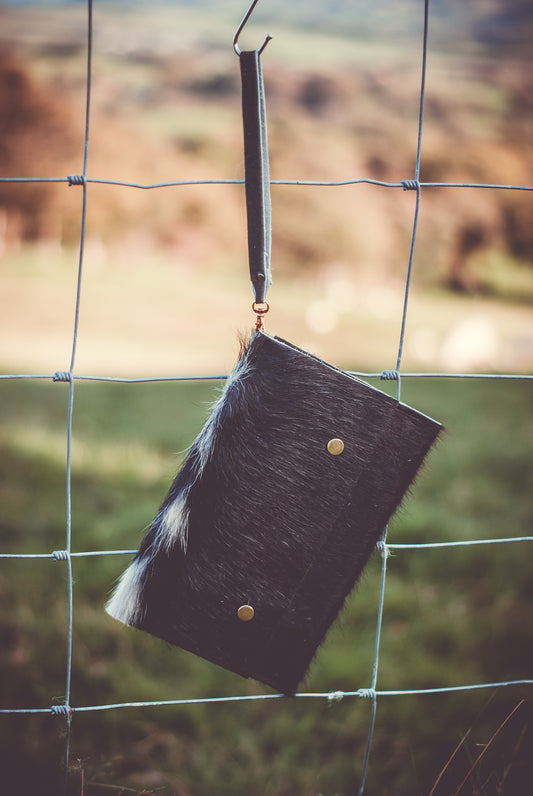 Cowhide clutch bag with fur-trim flap, brass snap buttons, hanging loop strap.