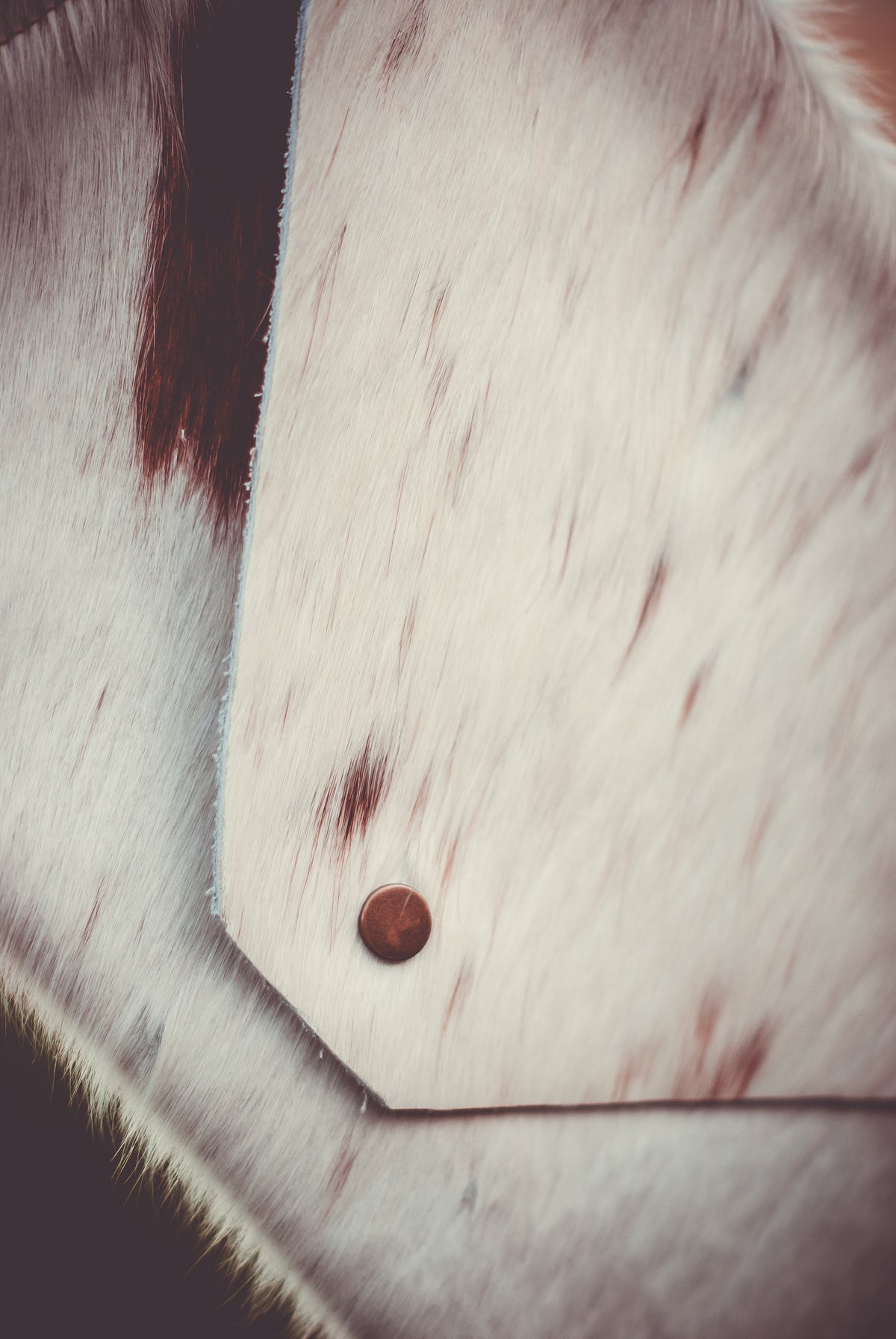 Cowhide clutch bag close-up, light fur with brown hide patch and button
