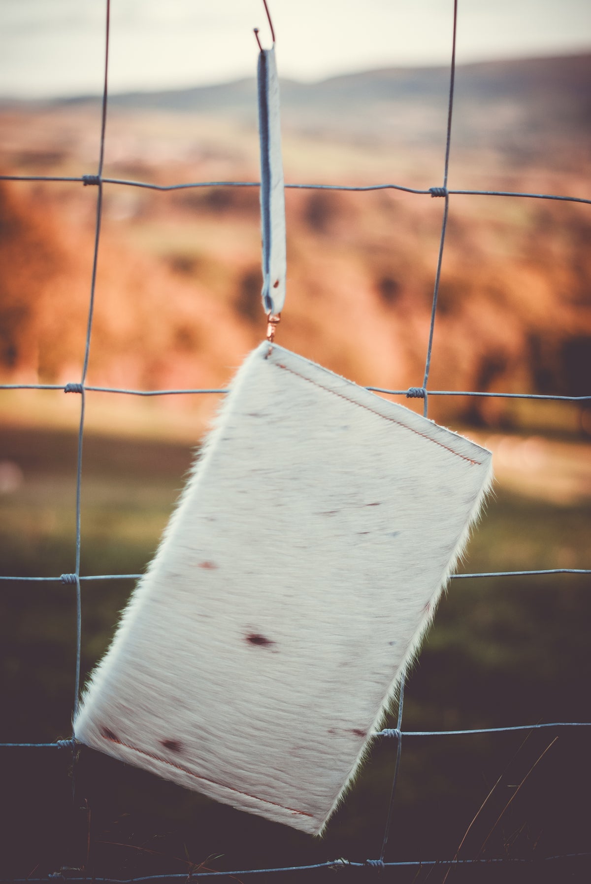 Cowhide envelope clutch bag with wrist handle, light fur and scattered dark markings