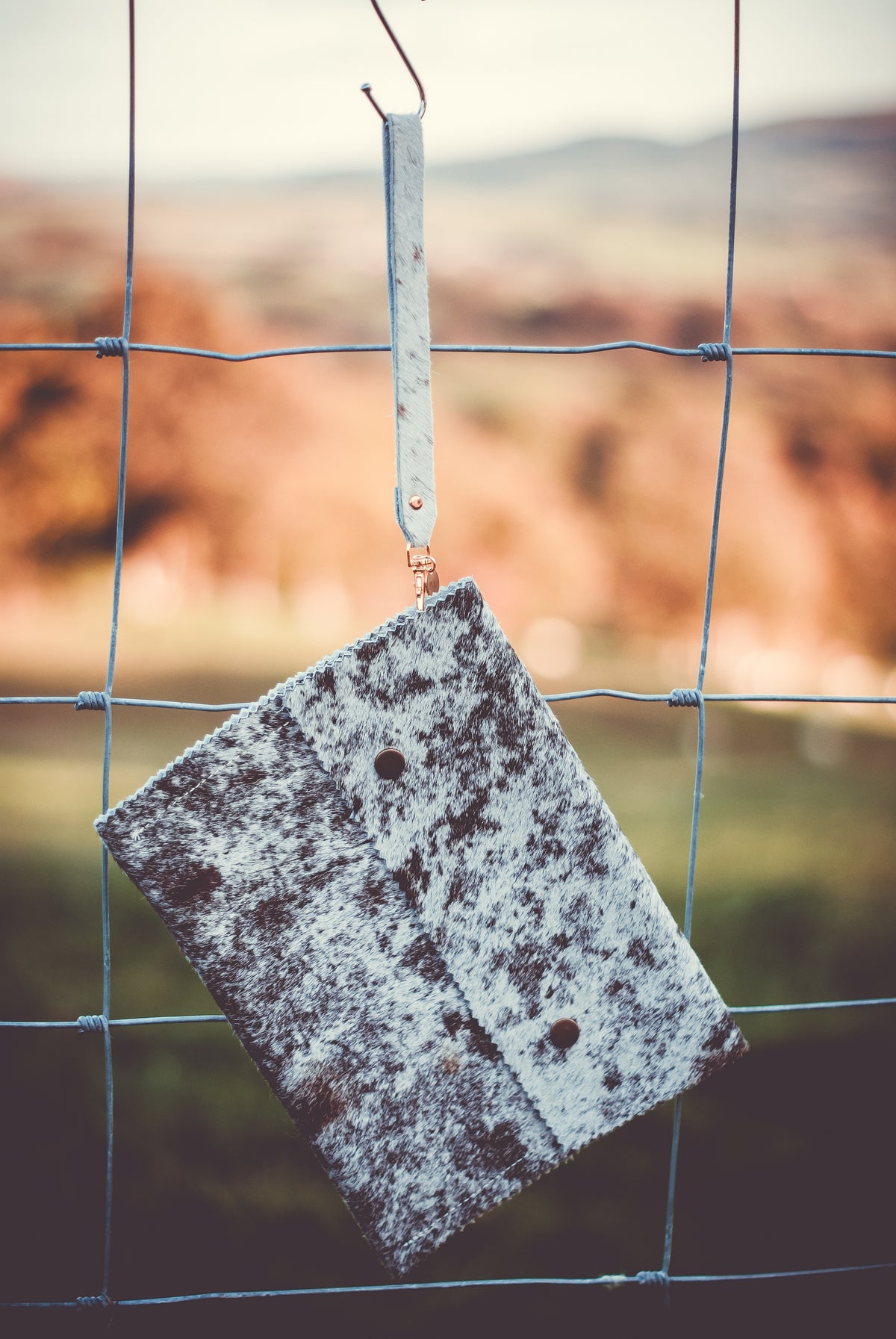 Cowhide clutch bag in mottled dark and light gray, with wrist strap and flap button.