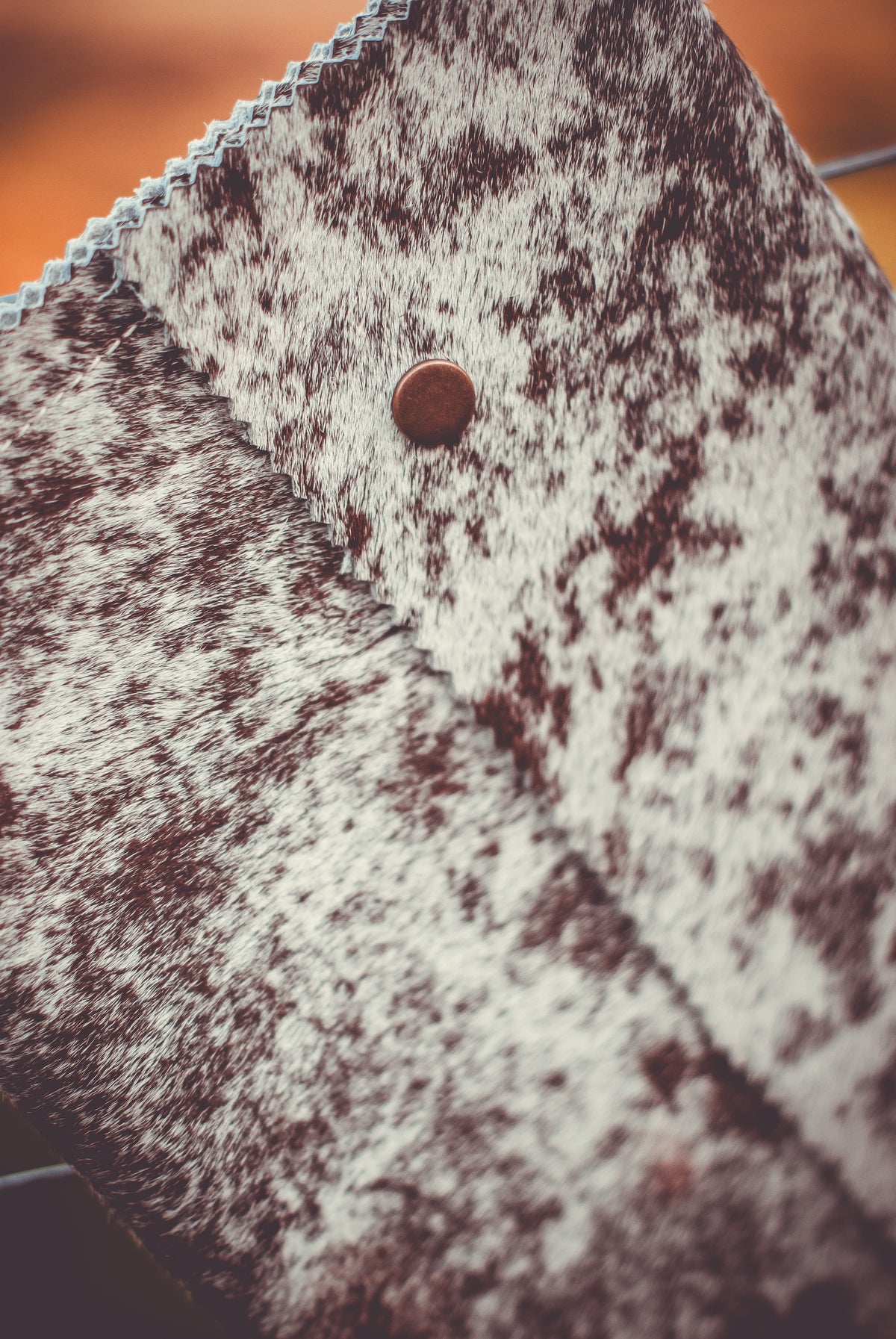 Cowhide clutch close-up: speckled gray flap with round button closure.