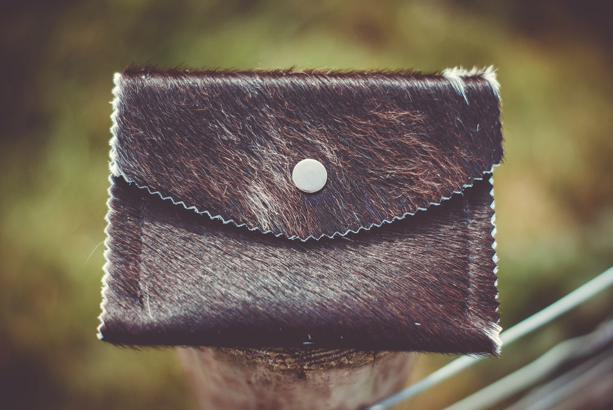 Small dark cowhide purse with flap and round white snap button, stitched edge