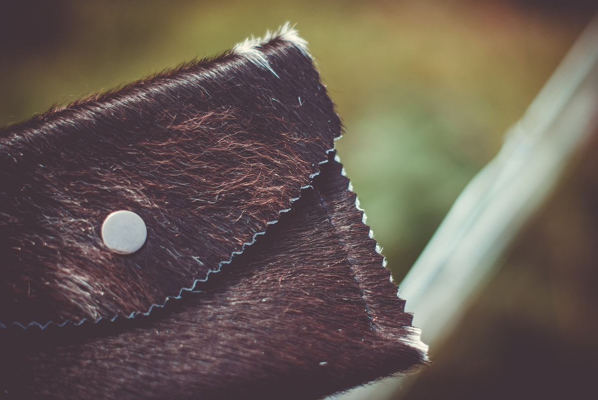Close-up of dark cowhide flap with zigzag stitched edge and round white snap